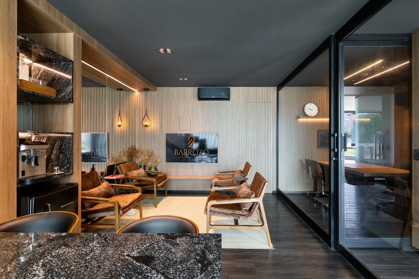 Lounge de espera da Barrozo Advocacia, com poltronas de couro, cafeteria e a marca na parede